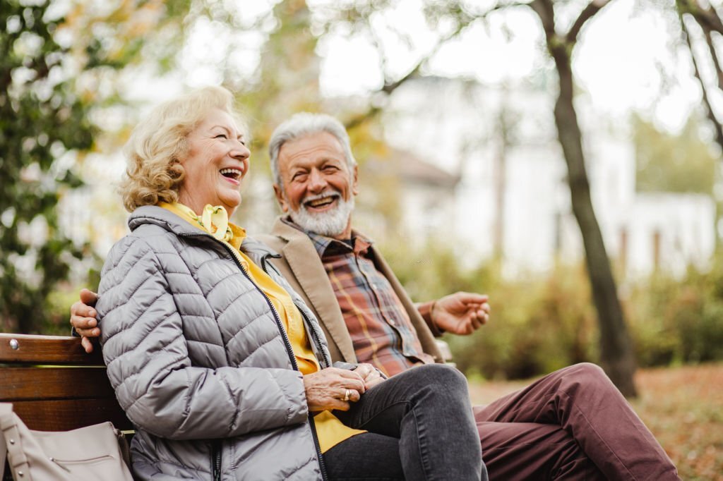 A happy senior couple sitting on a bench together in warm clothing